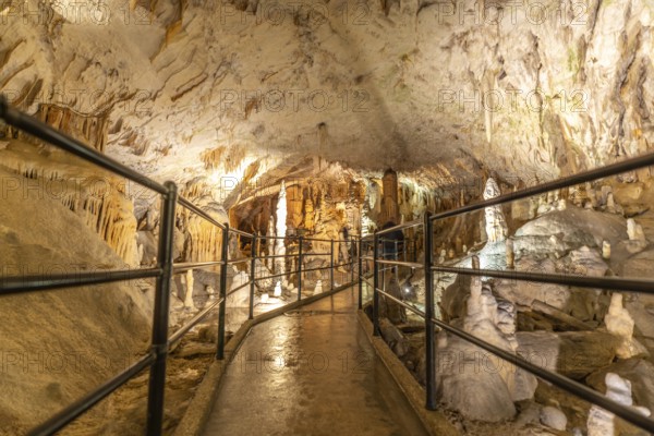 Tourists are enjoying a visit inside postojna cave in slovenia, walking on illuminated footpath