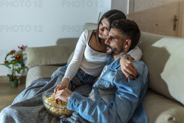 Romantic couple sharing a bowl of popcorn while watching a movie on television in their living room