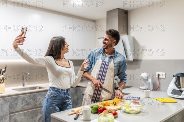 Young couple taking selfie with smartphone while preparing a healthy vegetarian salad in a modern