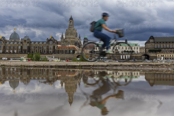 The Dresden silhouette with a cyclist and dark clouds behind the Church of Our Lady is reflected in