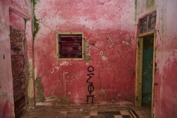 Pink-painted room with graffiti on the walls, exposed to severe decay and ageing due to damaged