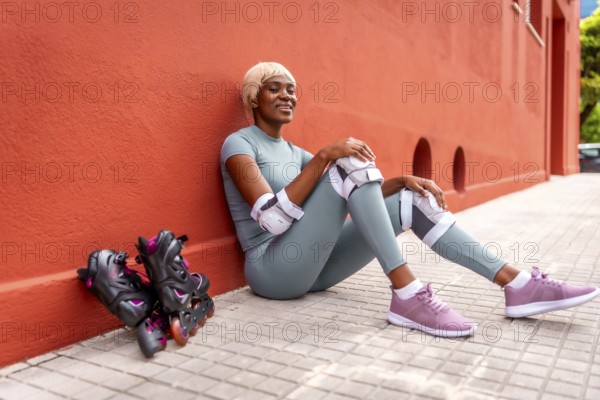 Beautiful african woman roller skating resting sitting on ground and leaning on red facade during