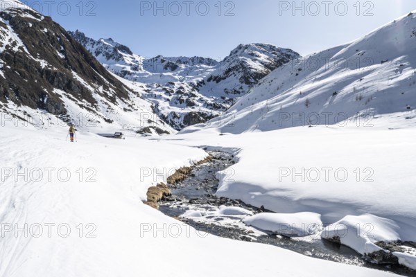 Ski tourer in the snow by a mountain stream in the Funtauna Valley, Graubünden Haute Route, Albula