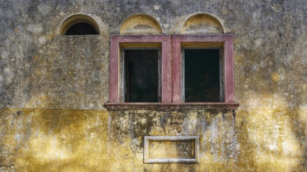 Two old windows in a dilapidated, yellow façade with heavily faded and peeling areas, Italian