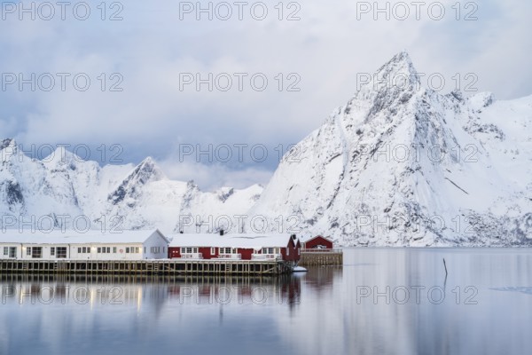 Rorbuer huts of Hamnoy at the fjord, snowy mountains in the background, Hamnøy, Reine, Moskenesøya,