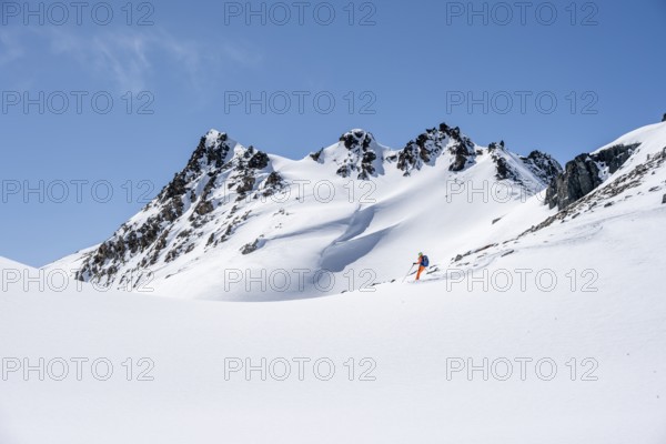 Ski tourer on the descent, minimalist winter landscape, white snow and dark mountains on the