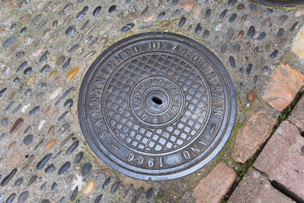 Manhole cover installed in Alquezar in 1966, surrounded by uneven paving stones, manhole cover,