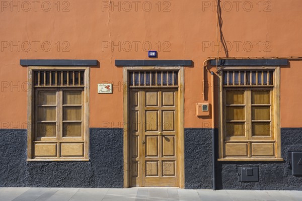 A building facade with an orange wall, wooden door, and windows. The base is painted black,