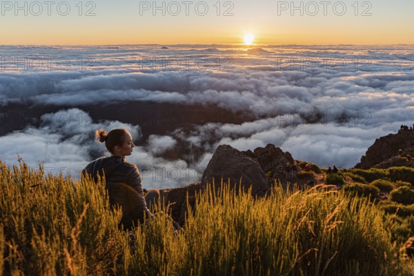 Woman sitting on a mountain watching the sunset over a sea of clouds, Pico Ruivo, Madeira,