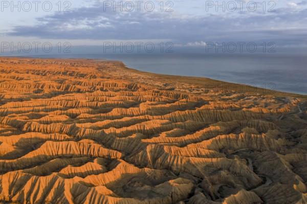 Landscape of eroded hills, badlands at sunset, Lake Issyk Kul in the background, aerial view,