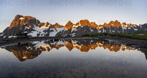 Rocky mountain peaks reflected in a small pond, mountain landscape with alpenglow at sunrise, at