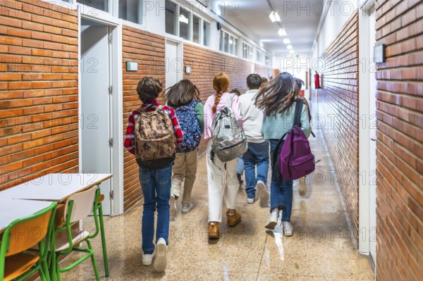 Rear view of elementary school students running down school hallway between classes, carrying