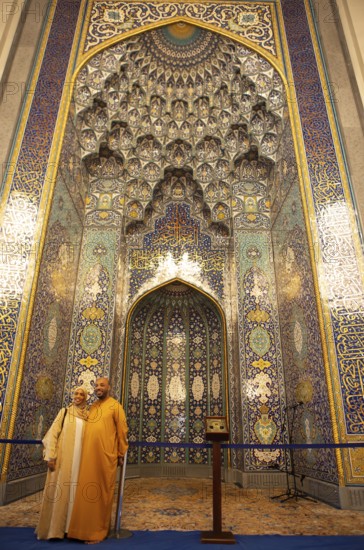 Omani couple in traditional dress in front of the golden prayer niche in the Sultan Qabus Grand