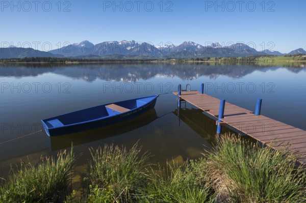 A jetty with a blue boat on a quiet lake with an impressive mountain view, Hopfen am See, near