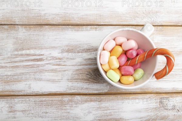 Heap of multicolored caramel candies in cup on white wooden background. copy space, top view, flat