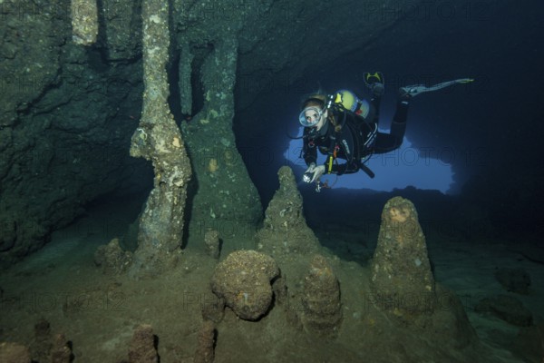 Scuba diver female diver swimming dives in entrance area of underwater cave stalactite cave