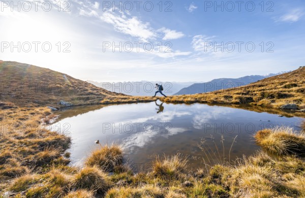 Mountaineer jumping, reflected in a small mountain lake on the Krahberg, mountain panorama in