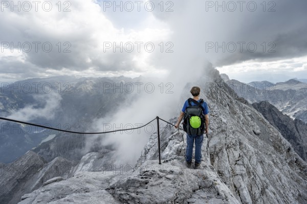 Mountaineer on a narrow rocky ridge on a steel cable, Watzmann crossing to Watzmann Mittelspitze,