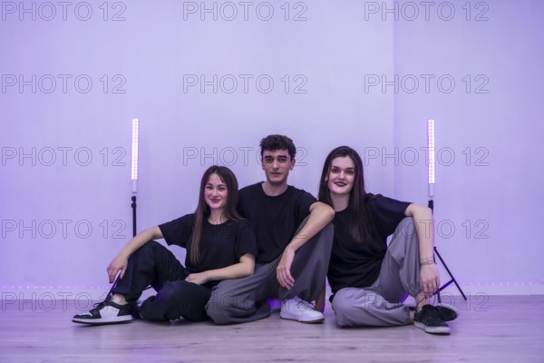 Three young dancers are sitting together on the floor of their dance studio, taking a break and