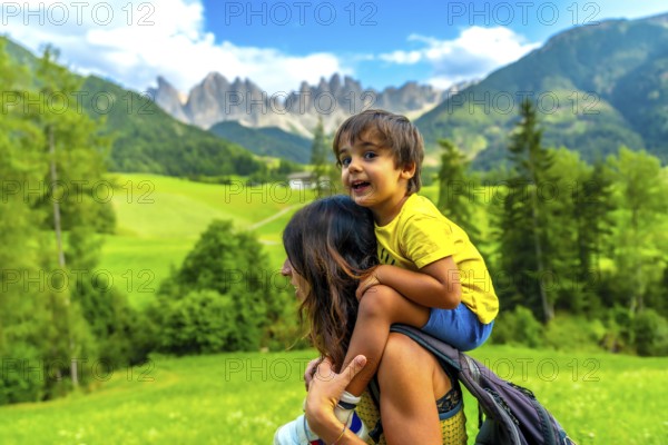 Mother carrying her son on her shoulders while enjoying the view of the odle mountains and the