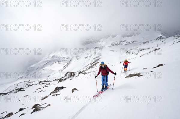 Two ski tourers in a wintry mountain landscape with cloudy mountain peaks, ascent to Piz Laviner,