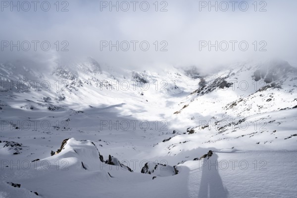View of cloudy valley from the summit of Piz Laviner, mountain landscape in winter, Grisons Haute