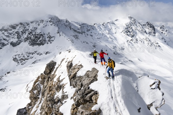 Three mountaineers climbing the narrow ridge of Piz Laviner, view of mountain panorama in winter