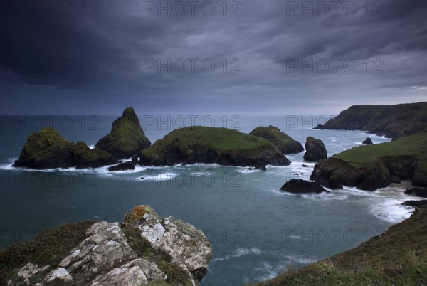 Dramatic clouds on rocky coast, rising rain shower over rocky islands with foaming surf, Kynance