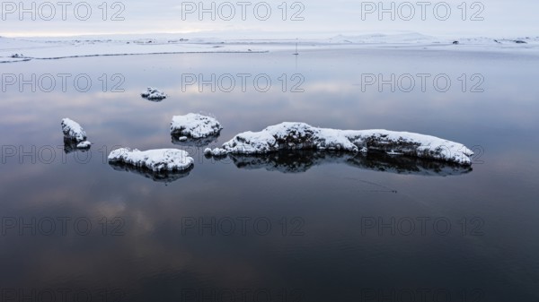 Snow-covered small islands overgrown with bushes in Lake Myvatn, at blue hour, Kalfaströnd, drone
