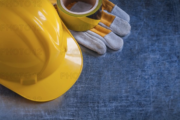 Safety tape yellow building helmet and protective gloves on scratched vintage metallic background