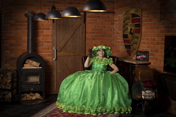 Woman in green dress sitting in a rustic room with fireplace and wood panelling, Staged photo