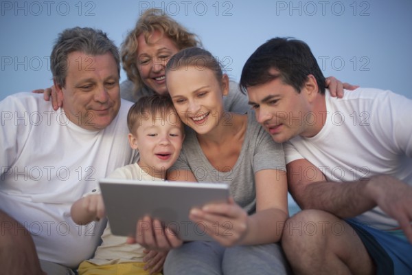 Happy big family having good time together. Grandparents and parents looking at the pad screen