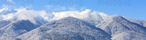 Winter travel vacation nature panoramic background with snow covered mountain peaks and blue sky