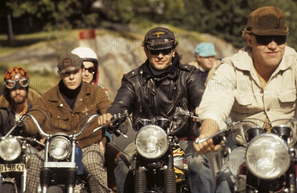 In the 1960s. Motorcyclists on the road together. Cool and trendy looking riding thir bikes. The