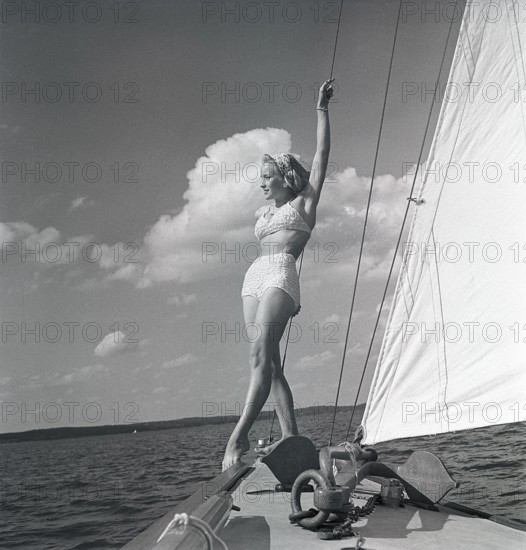 1940s sailing boat. A young woman is aboard a fashionable sailing boat and is standing on deck when