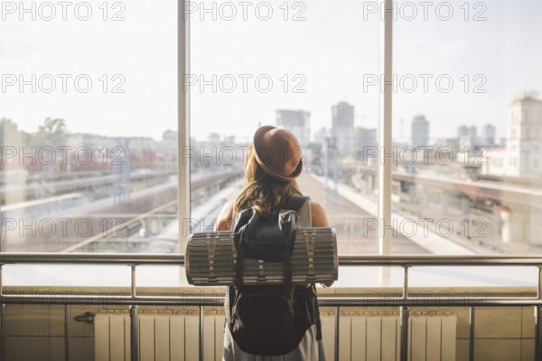 Traveler Rear view woman standing at the window in hall Train Station departure with backpack,