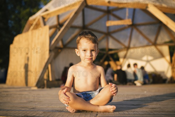 Theme is yoga and children. Caucasian Boy child sitting barefoot cross-legged in lotus position on
