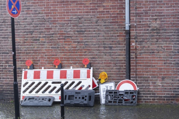 Red and white construction barrier, traffic signs, and bases stacked against a brick wall with no