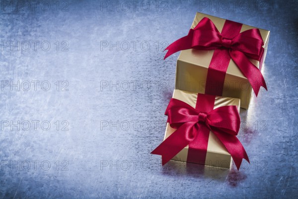 Boxed golden presents with red bow on scratched metallic background