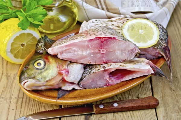 Bream whole peeled and cut into chunks in a clay plate, parsley, lemon, vegetable oil, napkin,