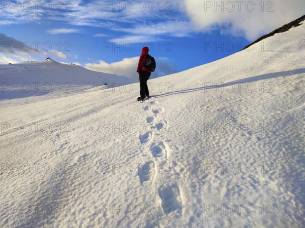 Person walking over snow-covered mountains, clear skies and footprints in the snow, Tromsø, Norway,