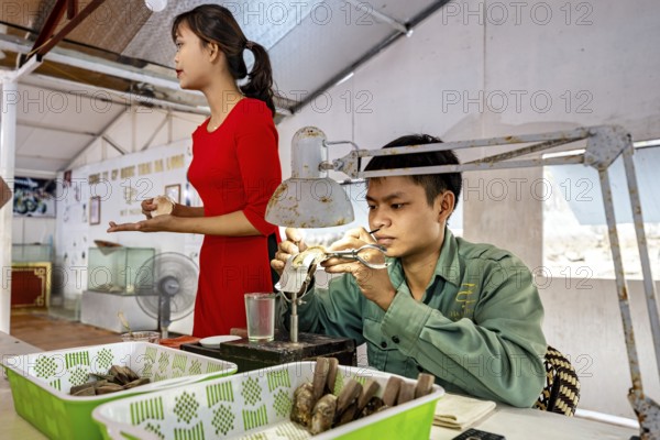 A man concentrates on his work while a woman stands next to him, pearl farm in Halong Bay, Vietnam,