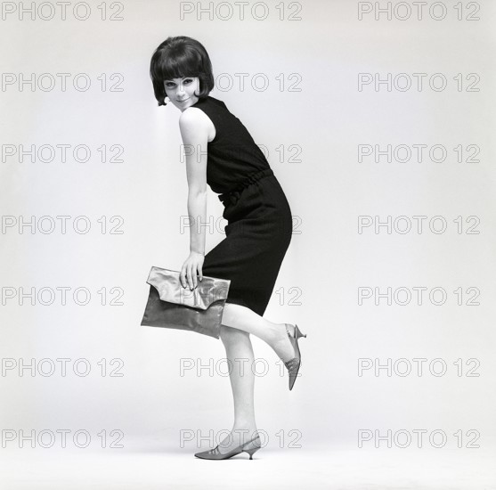 In the 1960s. A model in a typical 1960s outfit photographed in a studio. A black popular dress in