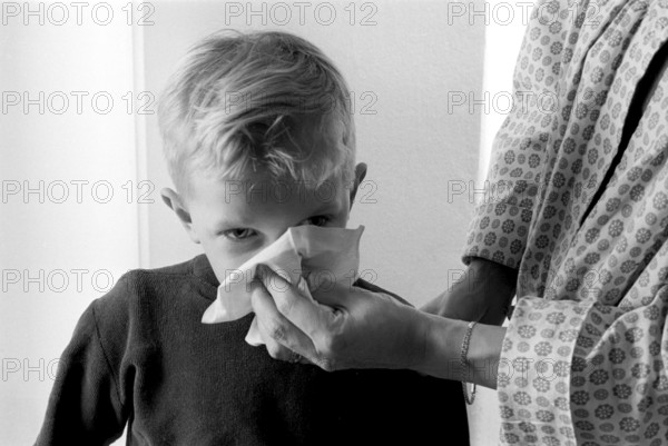 Boy in the 1950s. A mother holds a handkerchief over her sons nose as he blows his nose. Sweden