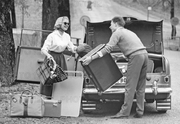 Couple in the 1950s. A young couple are packing the trunk of their car with luggage and camping