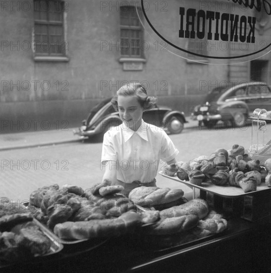 In the 1950s. A woman is pictured in the street and at the storefront of a bakery. She looks as if