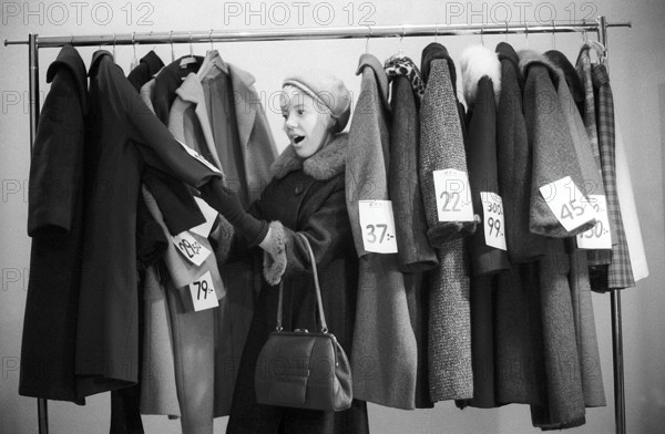 Great discounts of outerwear in the 1960s. A woman stands by a clothes rack, choosing from