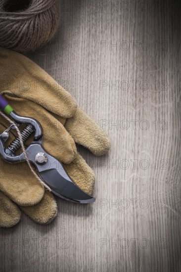 Pair of leather safety gloves sharp metal secateurs and skein of twine on wooden background