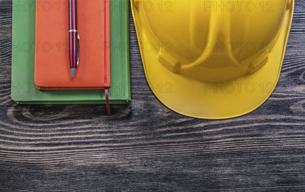 Note-books ballpoint pen protective building helmet on wooden board construction concept
