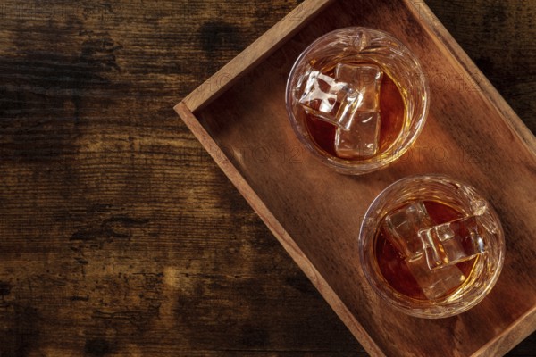 Whiskey in glasses with ice. Bourbon whisky on rocks on a dark rustic wooden background, overhead